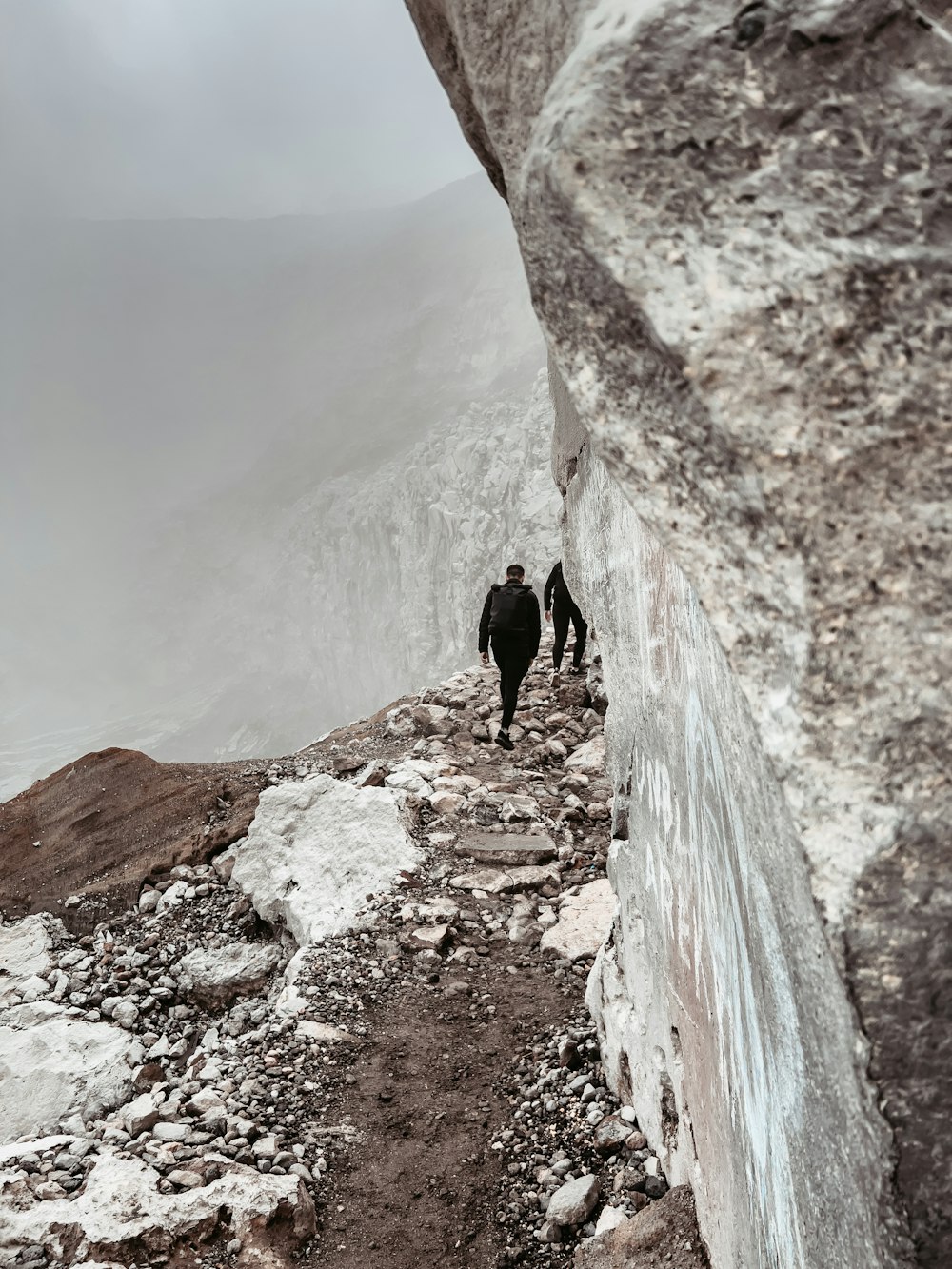 a couple people walking on a rocky path between mountains