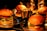 Four hamburgers are placed on metal trays, each containing lettuce, tomatoes, and sauce. A small bucket filled with french fries is also visible in the center, surrounded by the hamburgers. The setting appears to be dimly lit with a warm, inviting glow.