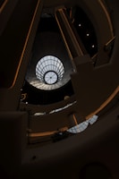 A modern architectural interior featuring a large circular skylight at the top, allowing natural light to stream in. The design includes multiple levels with sleek lines and a futuristic aesthetic. The structure appears symmetrical with metal and glass elements.