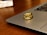 Two gold rings with embedded gemstones are placed on the edge of a laptop, which is set on a wooden surface. The light reflects off the rings, highlighting their shiny and intricate design.
