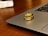 Two gold rings with embedded gemstones are placed on the edge of a laptop, which is set on a wooden surface. The light reflects off the rings, highlighting their shiny and intricate design.
