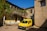 A bright yellow van parked in front of a rustic Italian building on a sunny day.