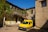 A bright yellow van parked in front of a rustic Italian building on a sunny day.