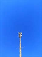 A cellular tower against a clear blue sky. The structure is tall and metallic with multiple antennas attached at the top.