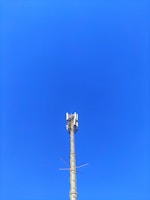 A cellular tower against a clear blue sky. The structure is tall and metallic with multiple antennas attached at the top.