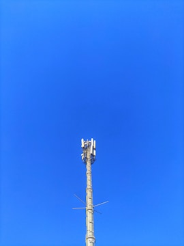 A cellular tower against a clear blue sky. The structure is tall and metallic with multiple antennas attached at the top.