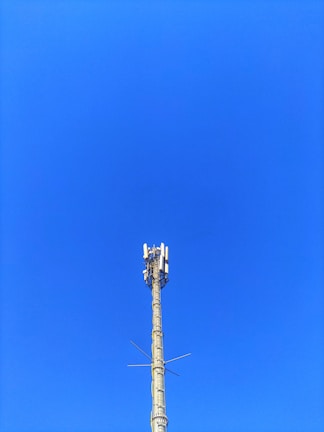 A cellular tower against a clear blue sky. The structure is tall and metallic with multiple antennas attached at the top.