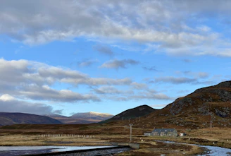 A peaceful rural landscape with green fields, a flowing river, and a cozy house under a bright sky.