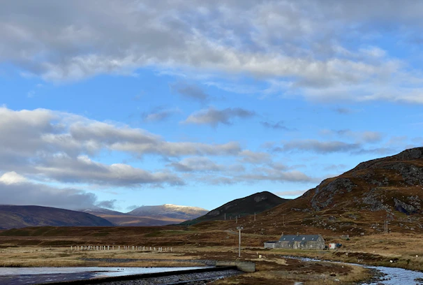 A peaceful rural landscape with green fields, a flowing river, and a cozy house under a bright sky.