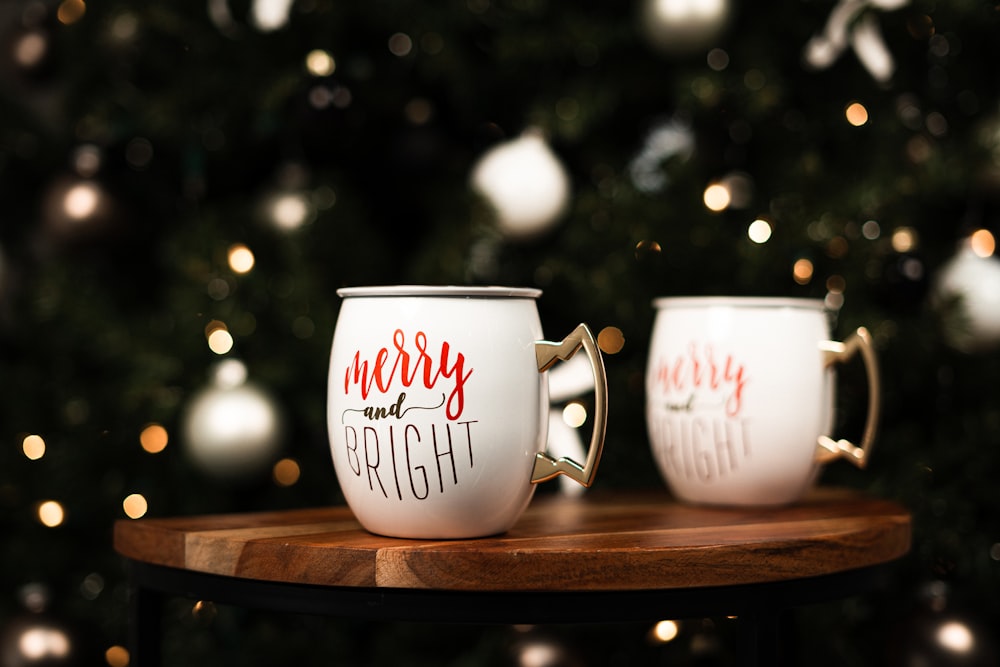 a couple of white mugs with red text on a wooden surface