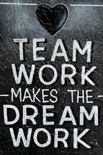 The image features the motivational phrase 'Team Work Makes The Dream Work' written in bold, white capital letters on a textured, dark background. A heart shape is positioned above the text, adding a positive and encouraging element.