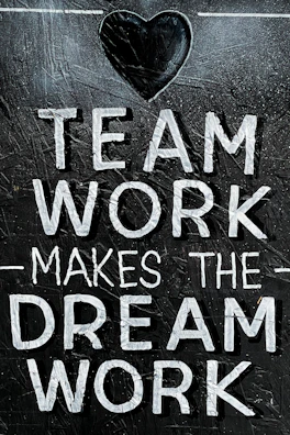 The image features the motivational phrase 'Team Work Makes The Dream Work' written in bold, white capital letters on a textured, dark background. A heart shape is positioned above the text, adding a positive and encouraging element.