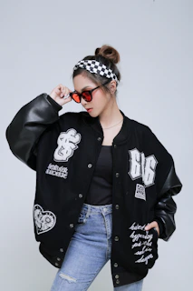 Model showcasing a casual look with a dark bomber jacket and fitted jeans, posing with relaxed confidence.
