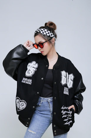 Model showcasing a casual look with a dark bomber jacket and fitted jeans, posing with relaxed confidence.
