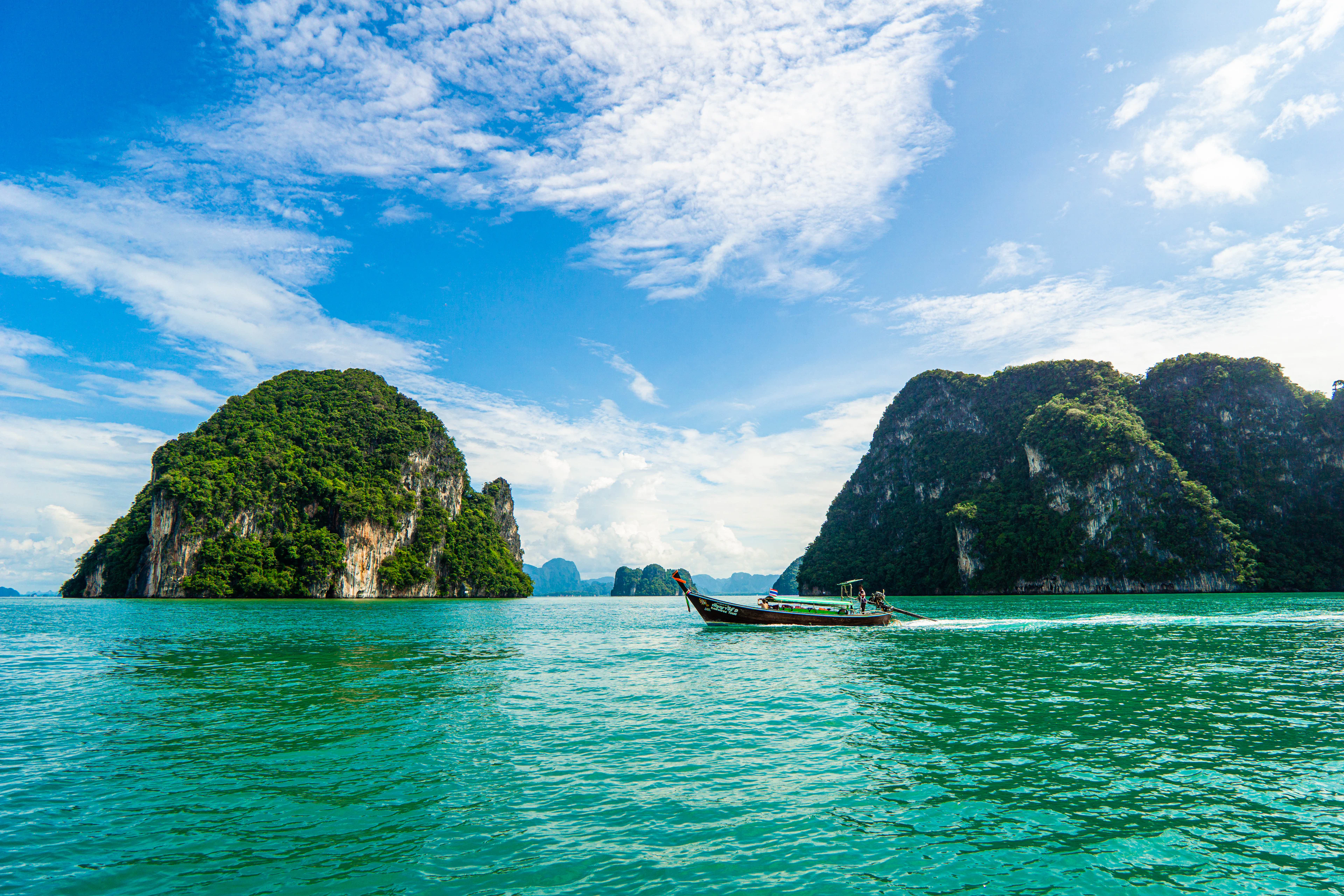 A longtail boat cruises a turquoise channel between two jungle-topped limestone islands near Krabi.