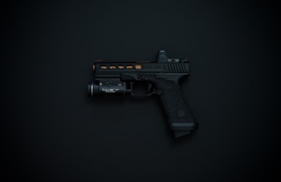 A black handgun with detailing and an attached flashlight is displayed against a dark background.