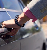 A professional chauffeur holding the door open for a business client in a suit.