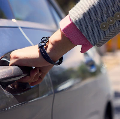 A professional chauffeur holding the door open for a business client in a suit.
