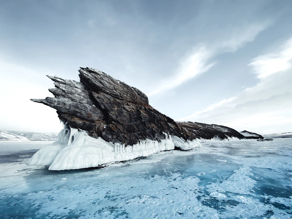 Large jagged rock formation with steep cliff face and frozen surface below it