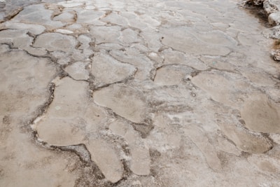 A close-up view of a surface composed of irregularly shaped, weathered stone-like formations. The surface appears to be natural, possibly a limestone or similar material, with varying shades of gray and beige. There are visible cracks and indentations that suggest erosion or natural weathering over time.