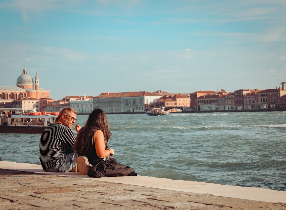 a man and woman sitting on a dock by the water