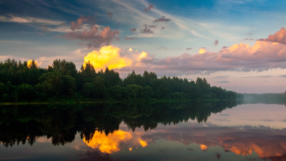 a body of water with trees and a sunset in the background