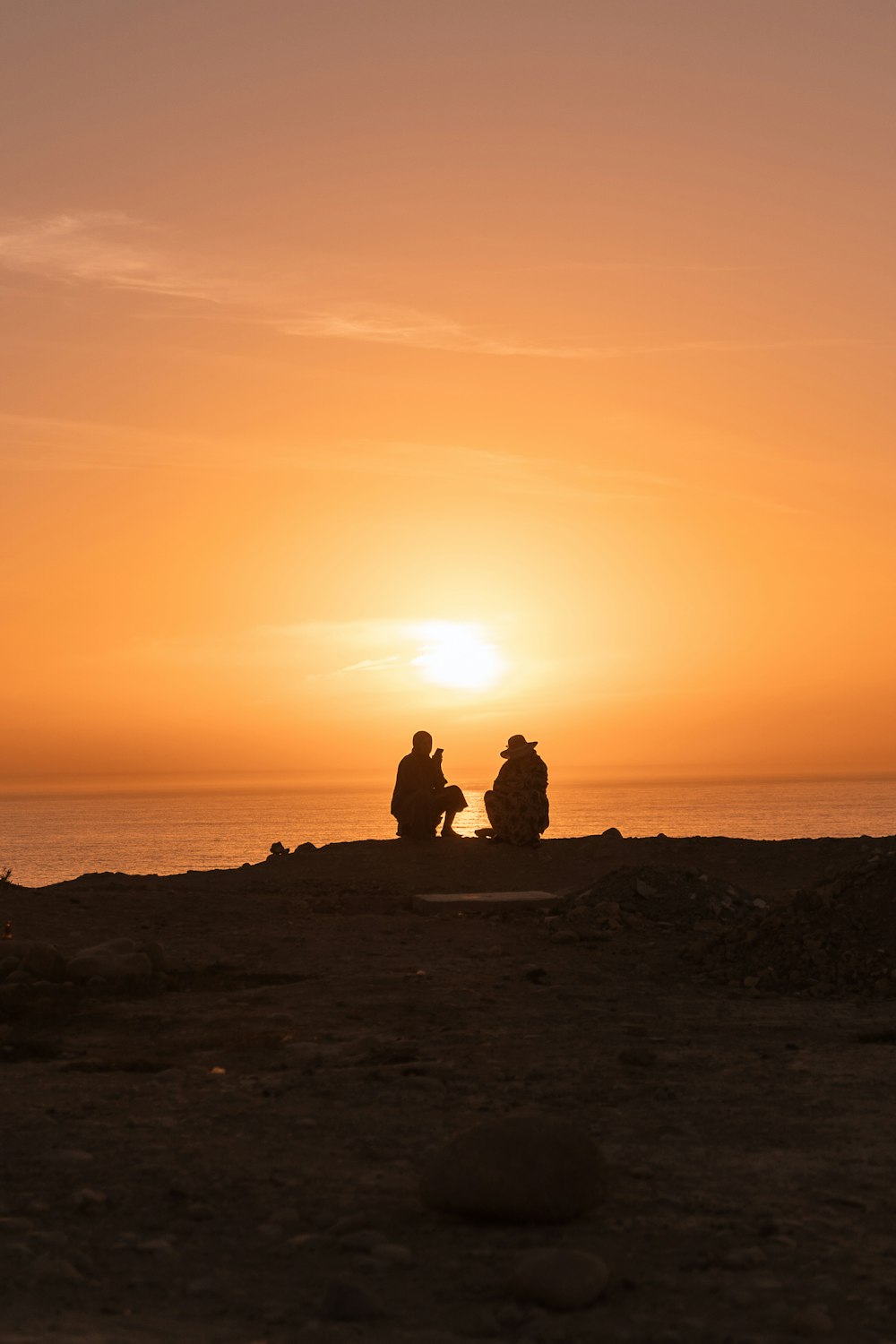 um casal de pessoas sentadas em uma rocha olhando para o pôr do sol