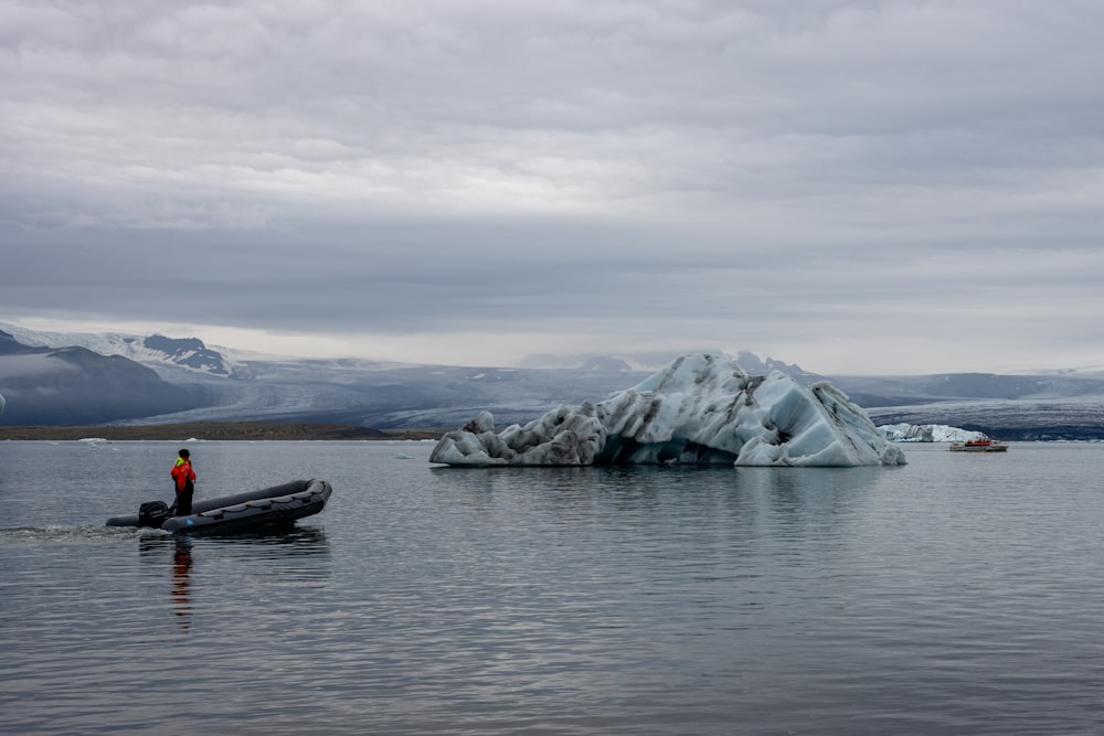 a person in a boat in the water with an iceberg in the background