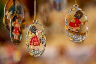Hanging decorations featuring small angel figures in red attire, with golden wings and accents, are suspended from strings. The delicate designs are oval-shaped and intricately detailed, with one angel holding a lantern.