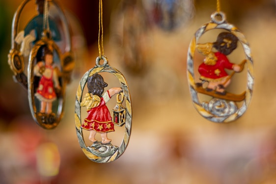 Hanging decorations featuring small angel figures in red attire, with golden wings and accents, are suspended from strings. The delicate designs are oval-shaped and intricately detailed, with one angel holding a lantern.