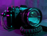 Close-up of a sleek camera lens with soft purple and blueberry blue neon glows, highlighting the precision of our photography gear.