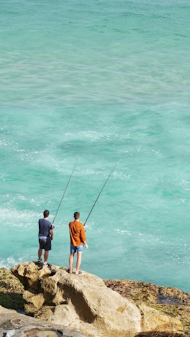 two men fishing on a rock