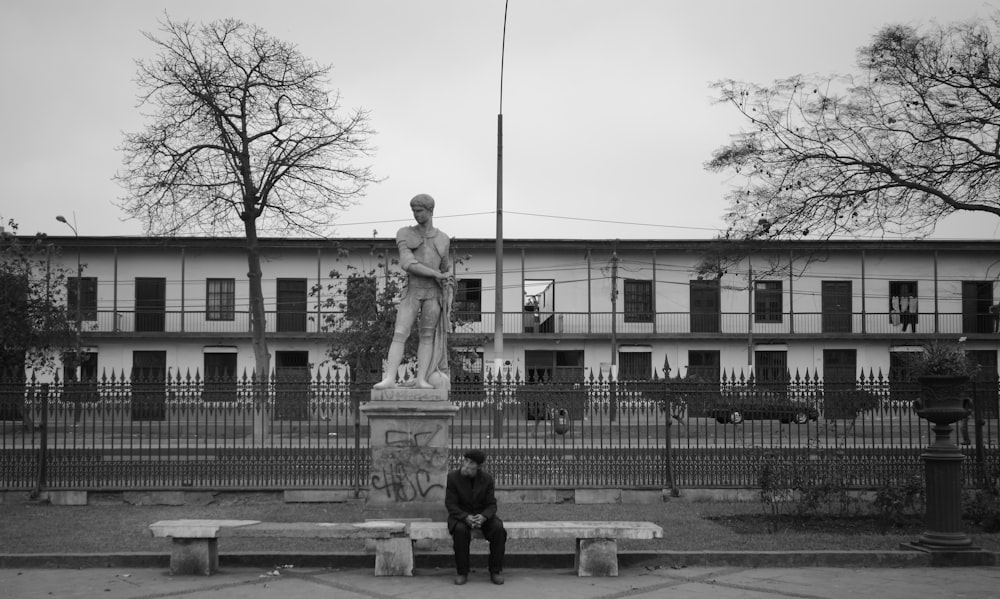 a person sitting on a bench next to a statue