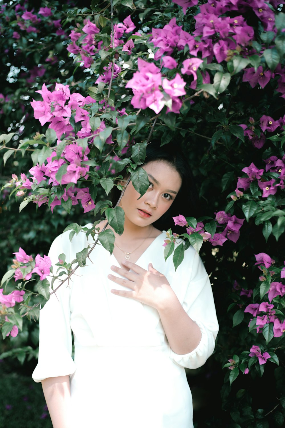 Una mujer posando frente a un arbusto de flores púrpuras