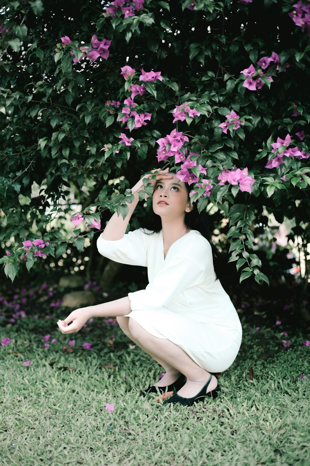 a woman sitting in a grassy area with flowers in the back