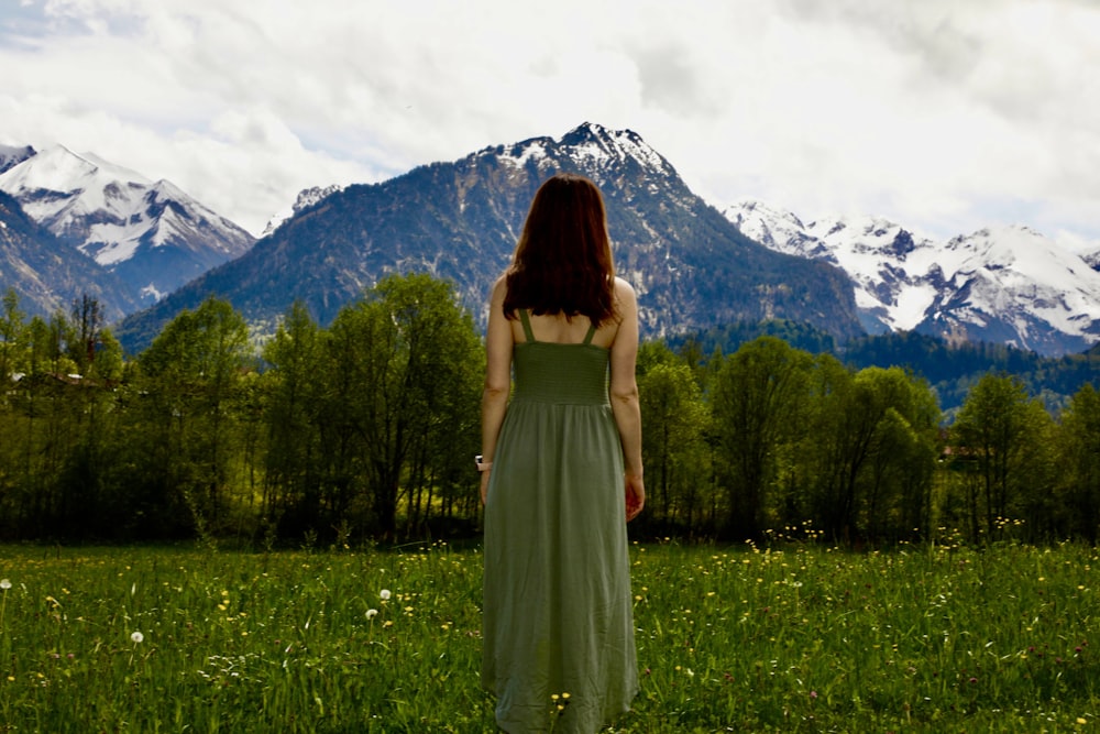 a person in a dress standing in a field with trees and mountains in the background