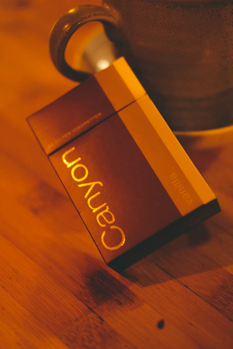 Close-up of a sleek pack of cigarettes resting on a wooden table with soft natural light highlighting the details.