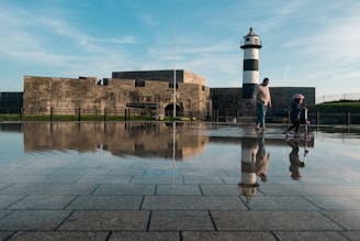a man and a child standing in a puddle of water with a lighthouse in the background