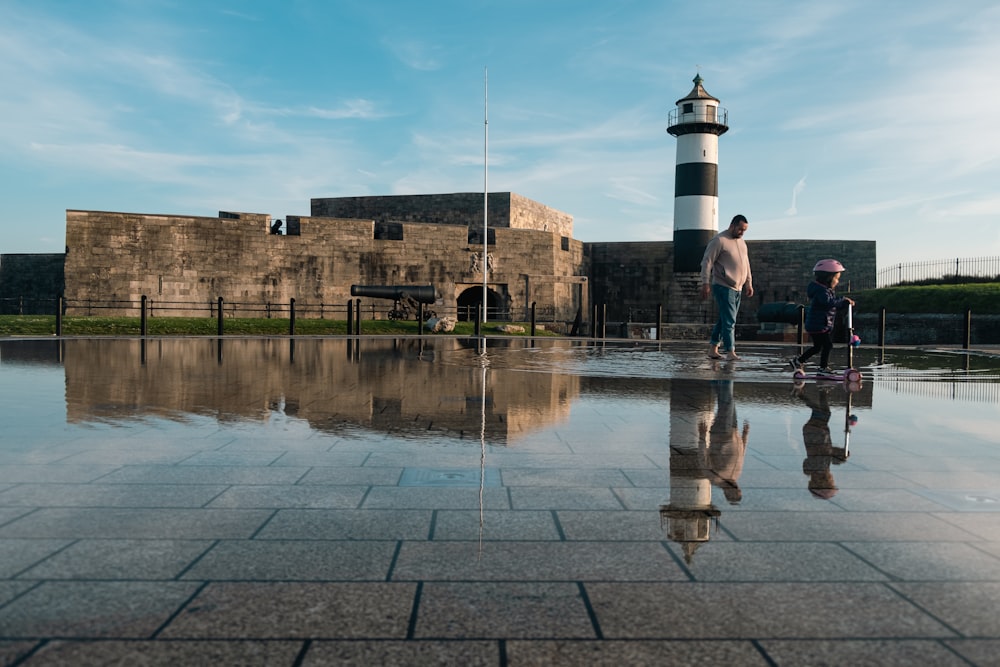 a man and a child standing in a puddle of water with a lighthouse in the background