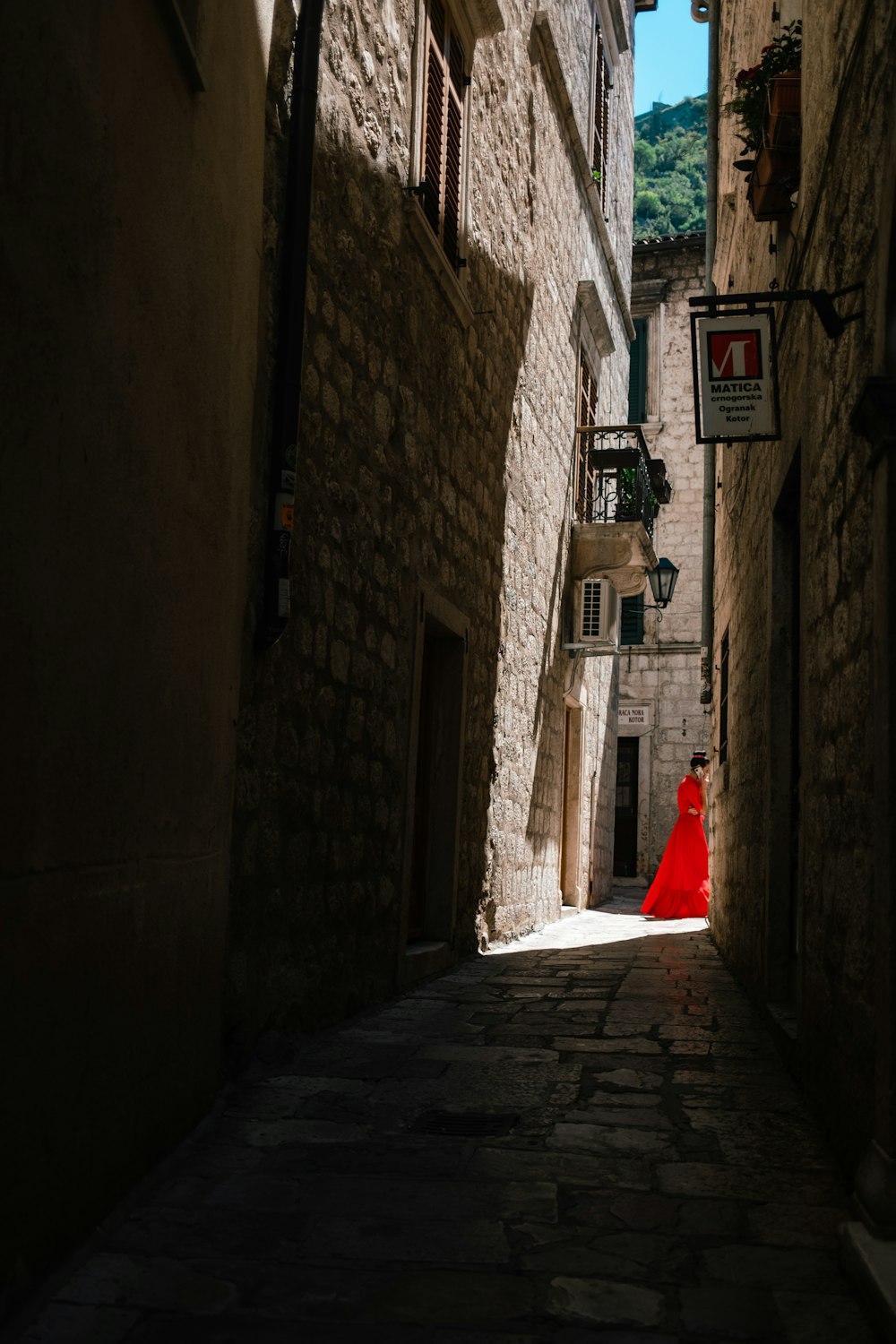 a person in a red dress walking down a narrow street
