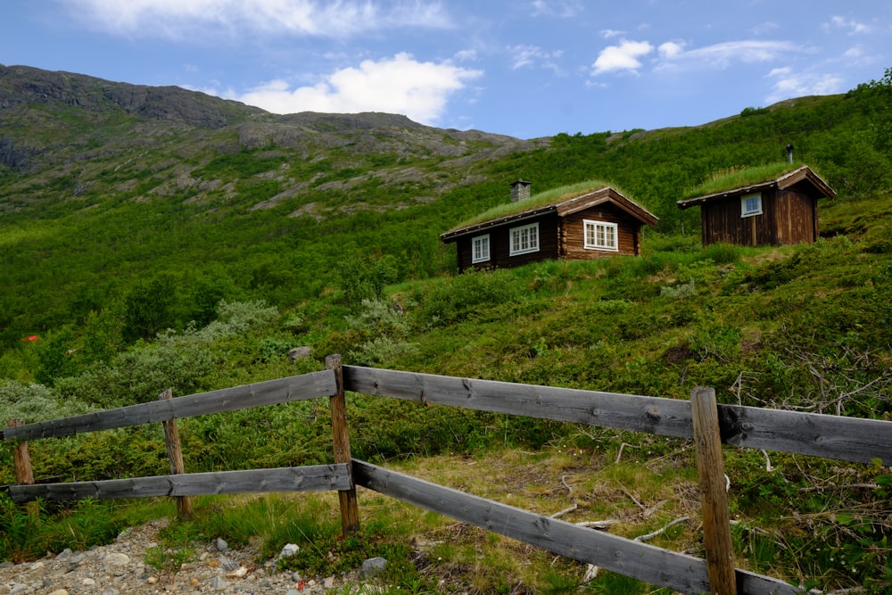 a wooden fence in front of a house on a grassy hill