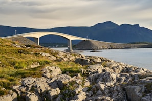 A sturdy concrete bridge arching over a flowing river with mountains in the background