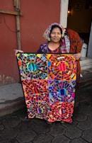 A Hmong woman artist smiling warmly as she displays her finished textile piece.
