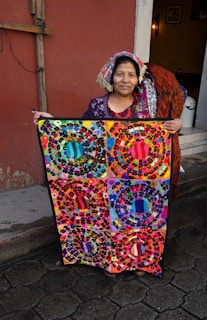 A Hmong woman artist smiling warmly as she displays her finished textile piece.