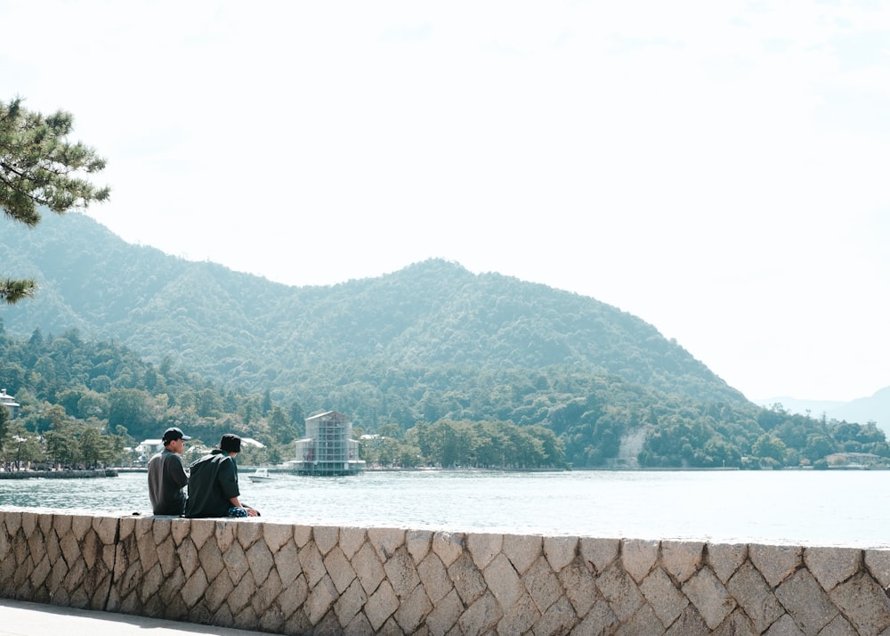 a couple sitting on a stone wall looking at a body of water