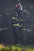 A firefighter in full protective gear handling a high-pressure hose amid smoke.
