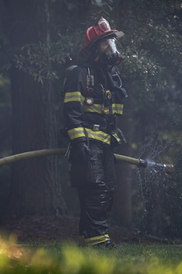 A firefighter in full protective gear handling a high-pressure hose amid smoke.