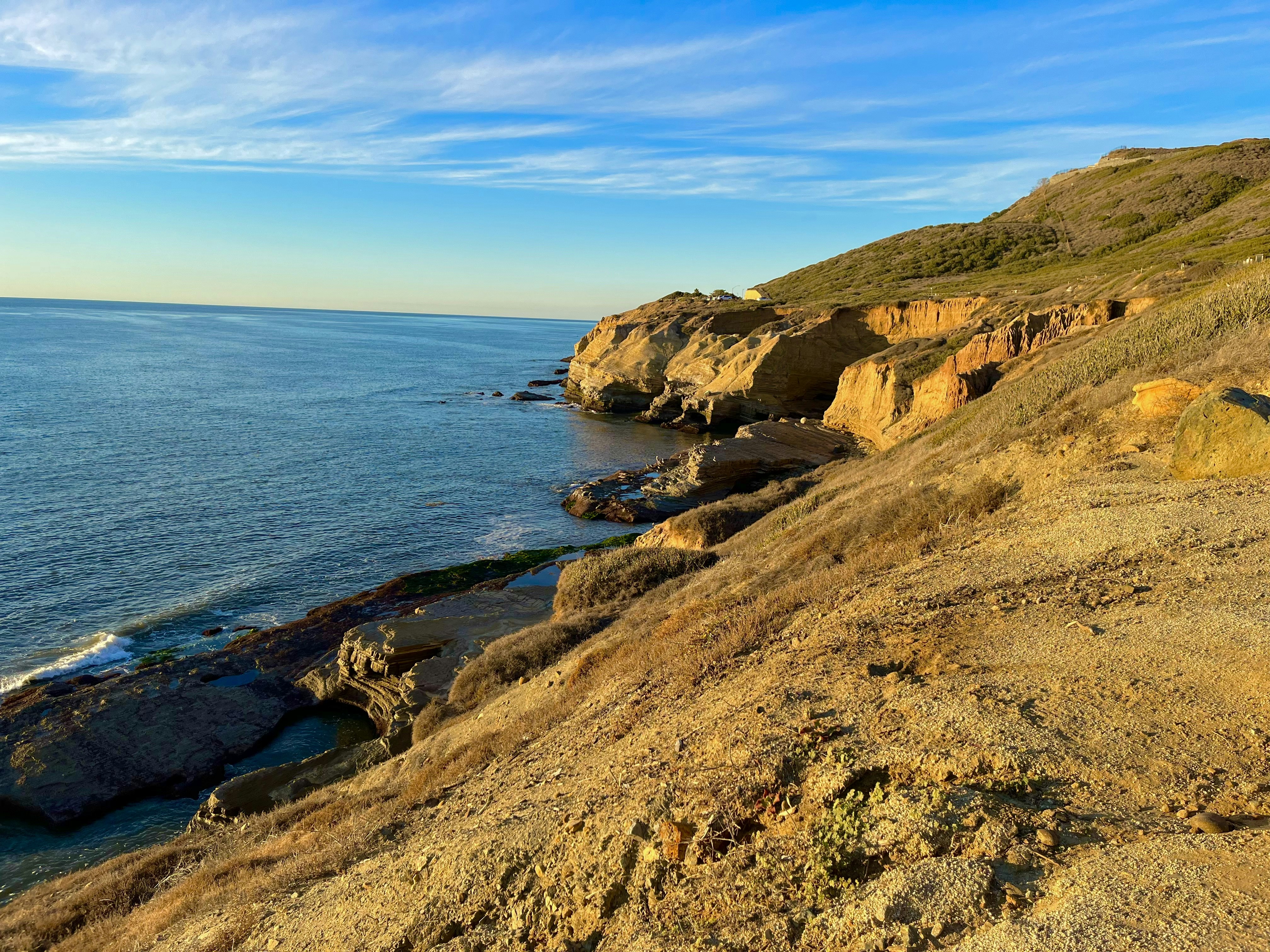 Coastal highway winding along sea cliffs at golden hour, dark ocean to left, dramatic sky with storm clouds on horizon, moody atmospheric light