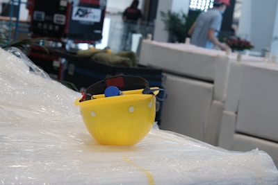 Close-up of yellow construction helmet resting on a stack of blueprints next to safety gloves.