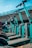 A row of teal-colored electric scooters lined up in an outdoor setting under a clear sky. The scooters are neatly arranged, and a concrete overpass is visible in the background, creating an urban environment.
